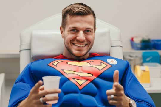 Mann in Superman Kostüm auf Blutspende Liege
