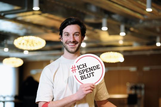 Junger Blutspender mit Schild lacht in die Kamera