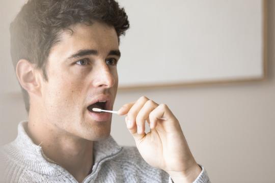 Junger Mann nimmt mit einem Stäbchen einen Mundhöhlenabstrich